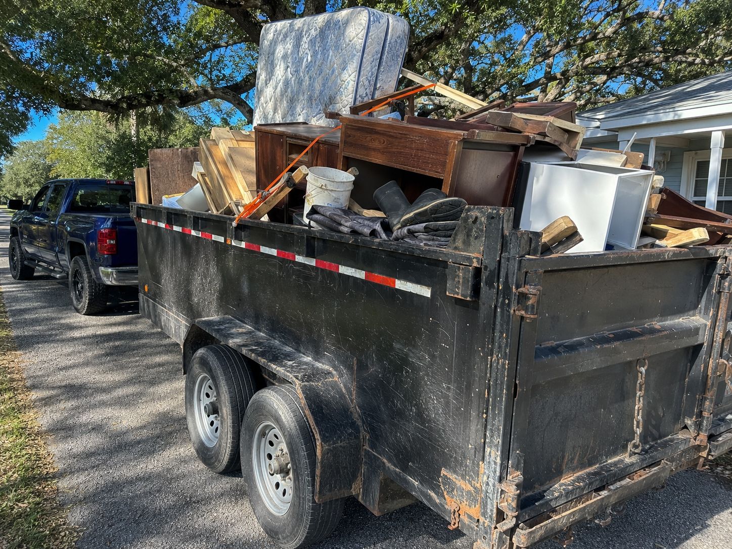 Dump trailer loaded with a mattress, dressers, and cabinets behind the truck on a driveway