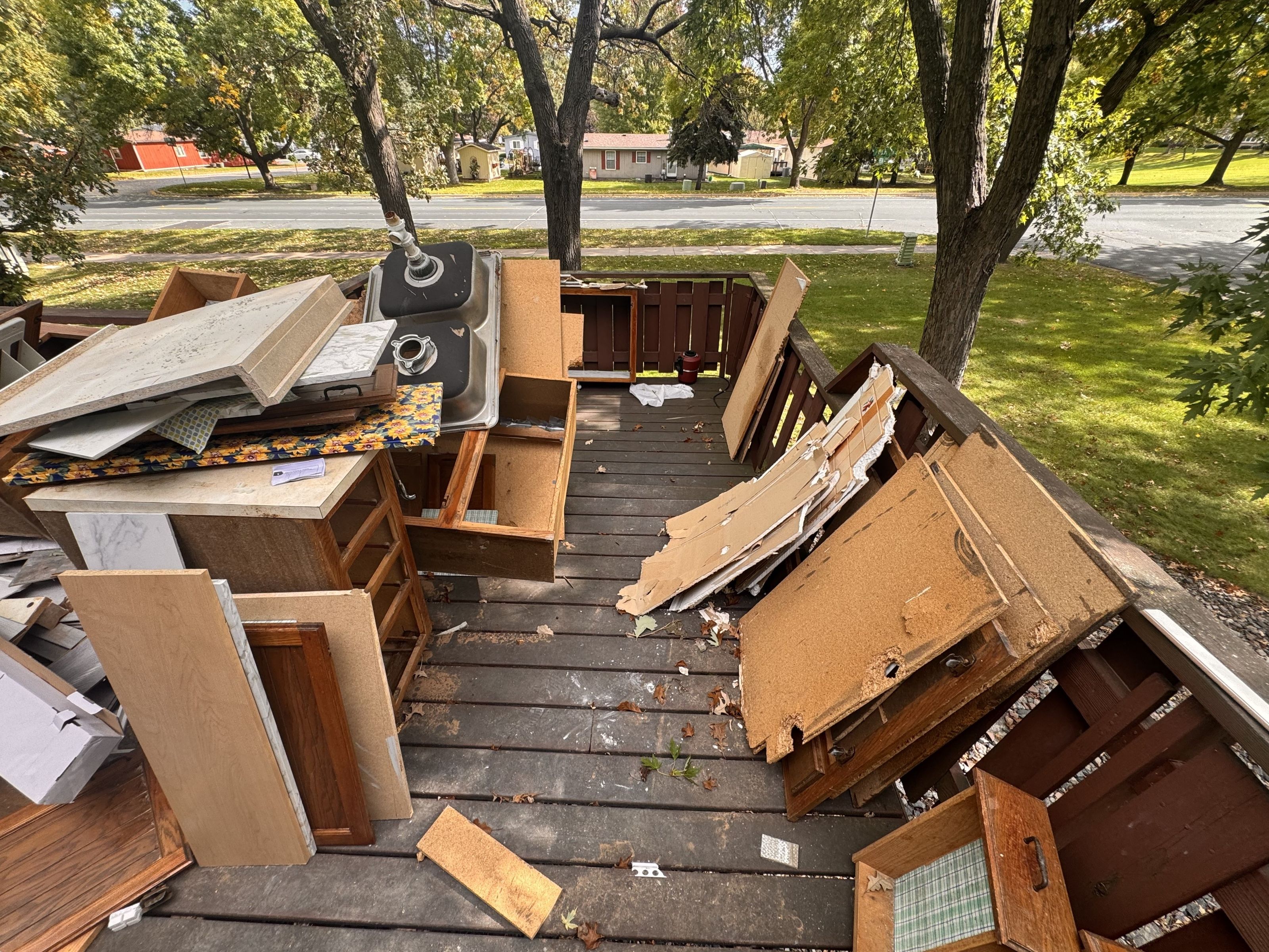 Torn-out kitchen cabinets, countertops, and a sink stacked for renovation debris removal
