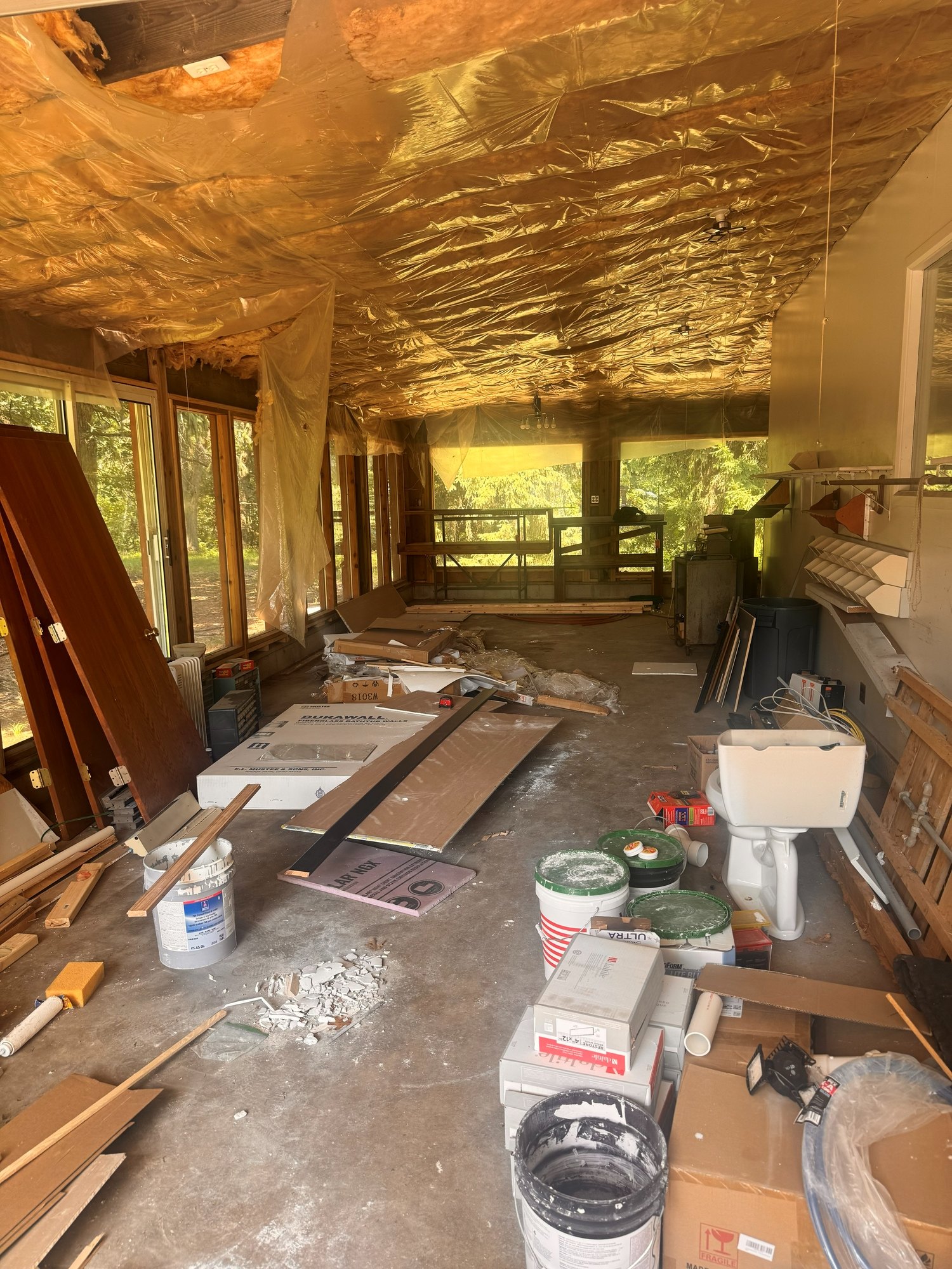 The same sunroom filled with lumber, buckets, and renovation debris before removal
